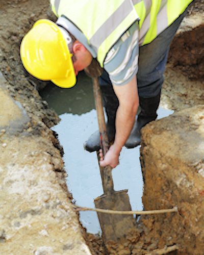 worker digging in a wet ditch with an exposed wire