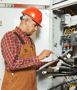 Electrical Worker standing at panel with clipboard.