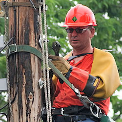 Electrician working on power line pole with adequate PPE.