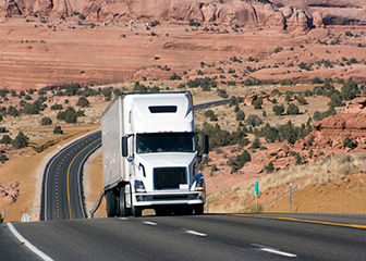 Big rig driving on empty highway through desert area.