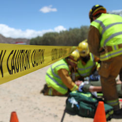 Accident scene being investigated by three people. Road is blocked with caution tape and cones.