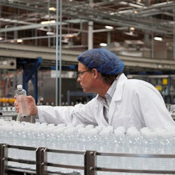 worker stretching to reach a bottle  while working at an assembly line