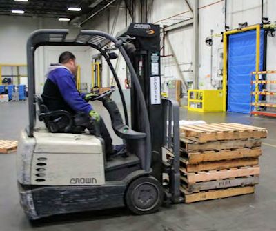 operator driving an electric forklift picking up a load of pallets
