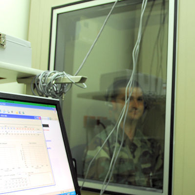 Patient sitting behind sound proof window while receiving a hearing test