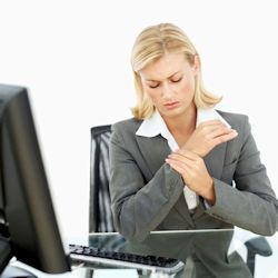 Image of woman sitting in chair in front of a computer rubbing sore wrist.