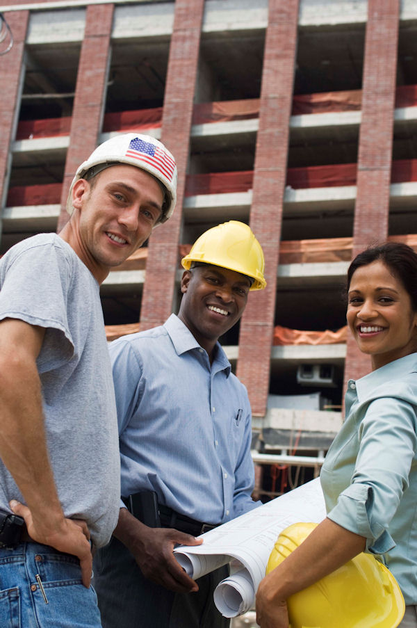 Three workers outside a building with blueprints.