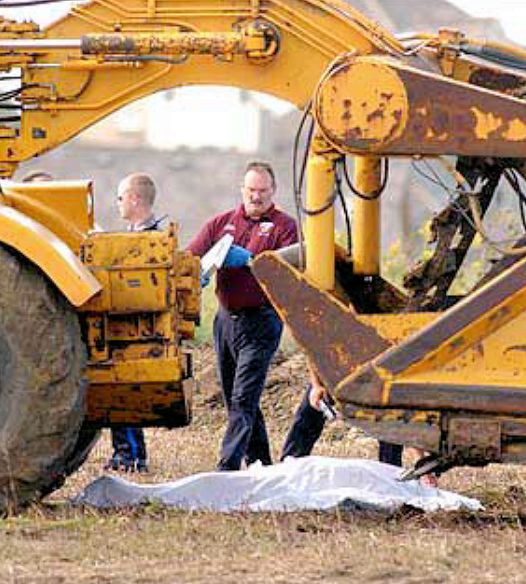 Under a giant backhoe a worker covering another employee with a cloth who has died.