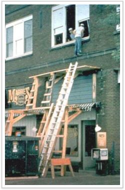 Lean-to scaffold with a worker climbing into a second floor window.