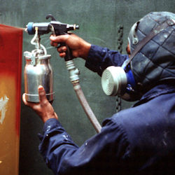 worker wearing PPE including a respirator spraying paint